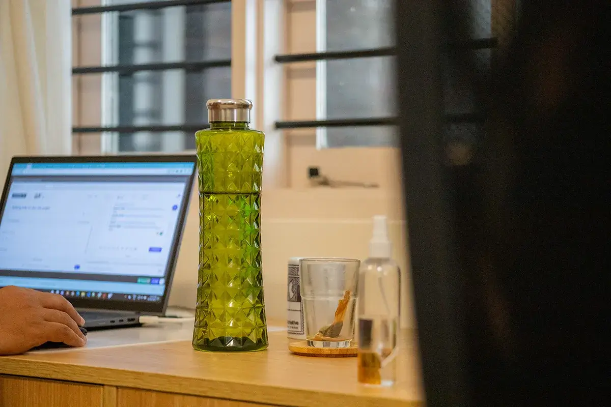 A green glass water bottle sitting on a desk