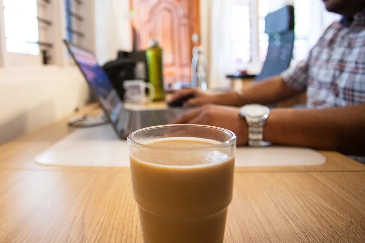 Drinking coffee at wooden desk while working on laptop